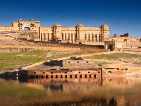1 The majestic Amber Fort in Jaipur, Rajasthan, rising against a clear blue sky, with its beautiful architecture reflected in the calm waters below.